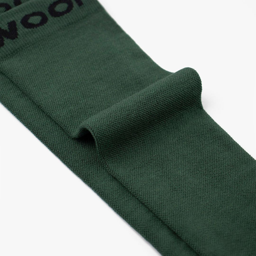 Macro close-up shot showing the Fern Green Bamboo Compression Socks folded flat to highlight the soft knit texture, smooth solid green weave, and dark "WOOF" top cuff band.   